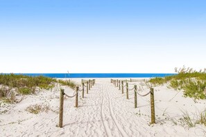 A sandy beach path leading to the ocean, with wooden posts and rope barriers.