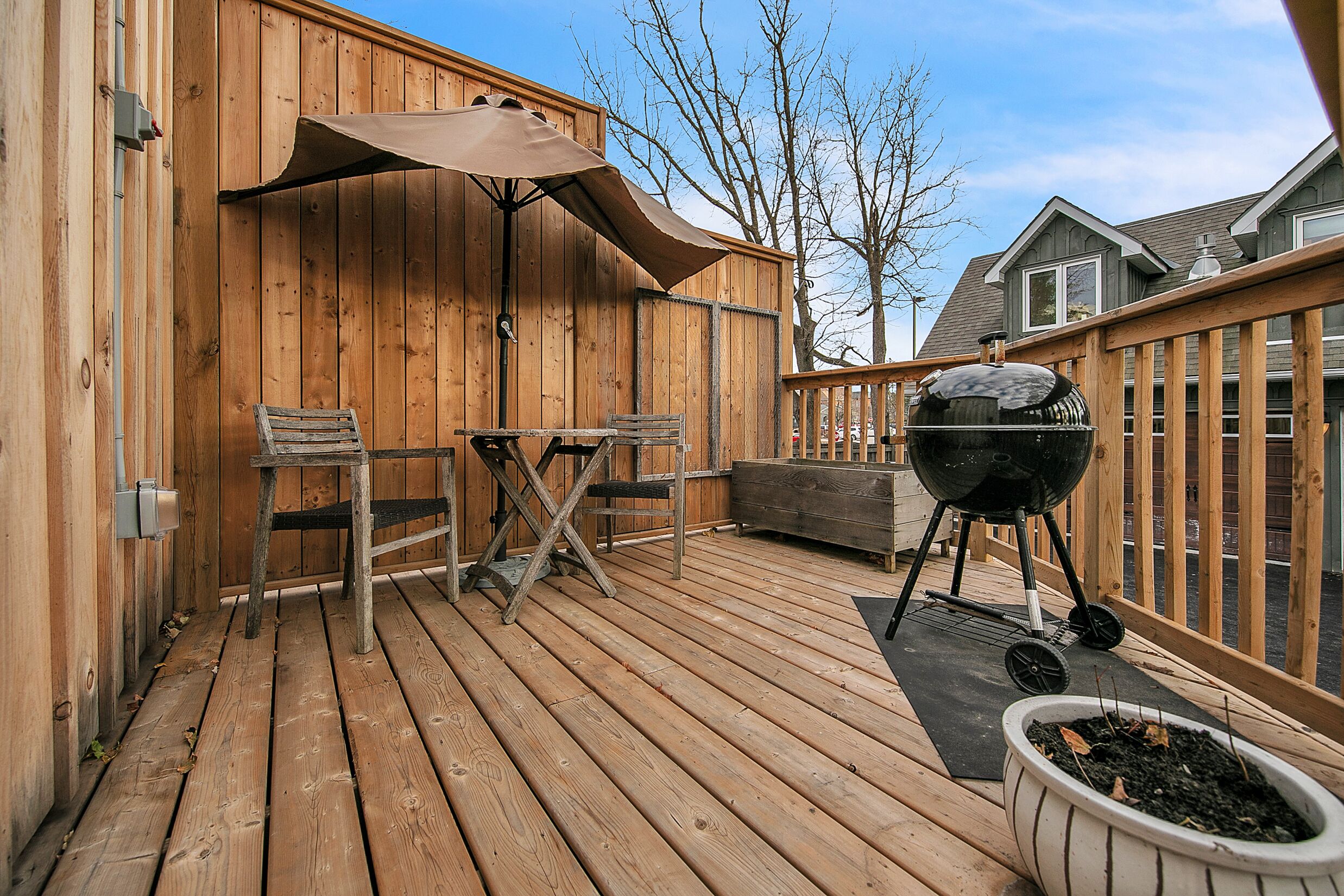 Une terrasse en bois avec un barbecue, une table et des chaises, et un parasol.