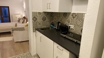 A compact kitchen with white cabinets, a black countertop, and patterned backsplash tiles.
