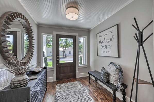 A modern interior with a wooden spiral staircase, a bench, a welcome sign, and a coat rack.