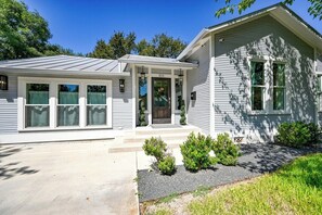 A single-story house with a front porch, a number '211' on the door, and a small garden with shrubs.