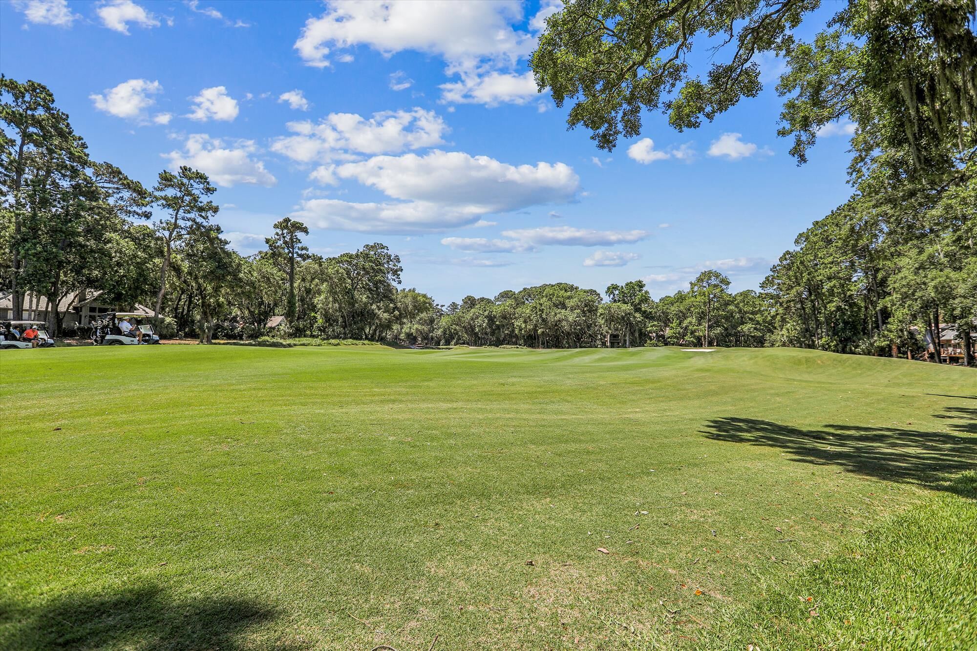 Ein Golfplatz mit blauem Himmel, Bäumen und einigen Personen.