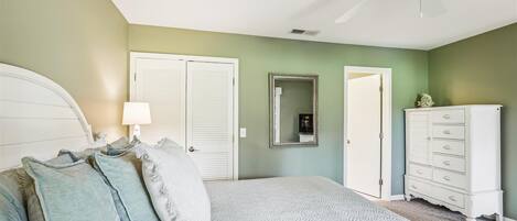 Un dormitorio con cama, cómoda, ventilador de techo y dos puertas.