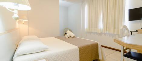 A hotel room with a bed, a desk, a telephone, and a television.