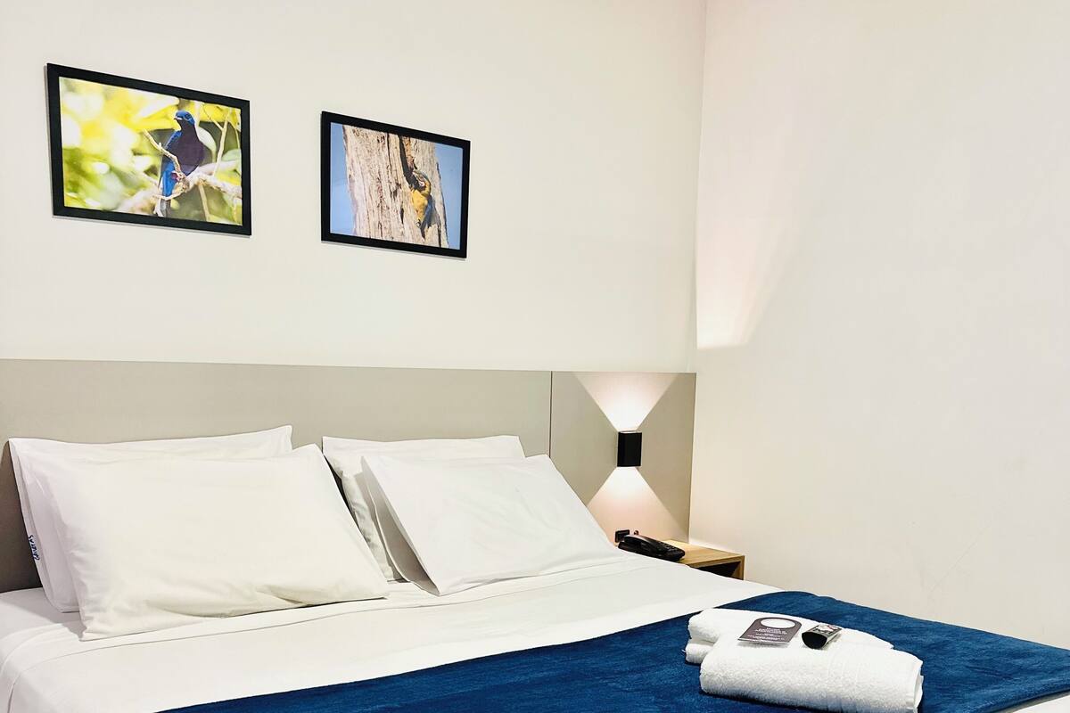 Une chambre d’hôtel avec un lit, du linge de lit blanc, un plaid bleu et deux tableaux encadrés accrochés au mur.