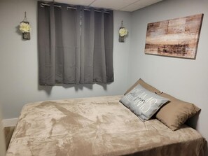A bedroom with a bed, grey curtains, a wall-mounted light fixture, and a painting. - Northern Wisconsin Waterfront Cabin Lake Ellwood Spread Eagle WI (Florence)