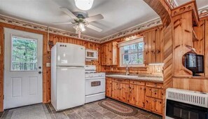 A kitchen with wooden cabinets, a refrigerator, stove, microwave, and a fireplace. - Northern Wisconsin Waterfront Cabin Lake Ellwood Spread Eagle WI (Florence)