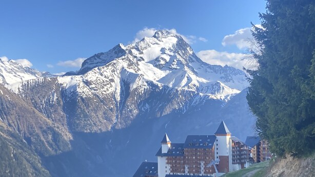 Una località montana con cime innevate, una seggiovia ed edifici in tipico stile chalet.