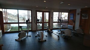 Una palestra con diverse attrezzature per esercizi, ampie finestre che offrono vista su un paesaggio innevato e pareti in legno.