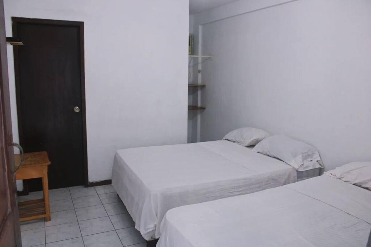 Una habitación pequeña y limpia con dos camas individuales, una silla de madera y una puerta.