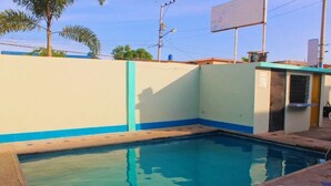 A swimming pool with a blue and white tiled edge, surrounded by a low wall and a small building with a window. - Hotel Manhattan Salinas Ecuador (Salinas)