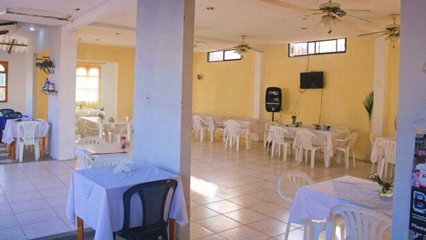 A spacious dining area with white tables and chairs, ceiling fans, and a television mounted on the wall. - Hotel Manhattan Salinas Ecuador (Salinas)