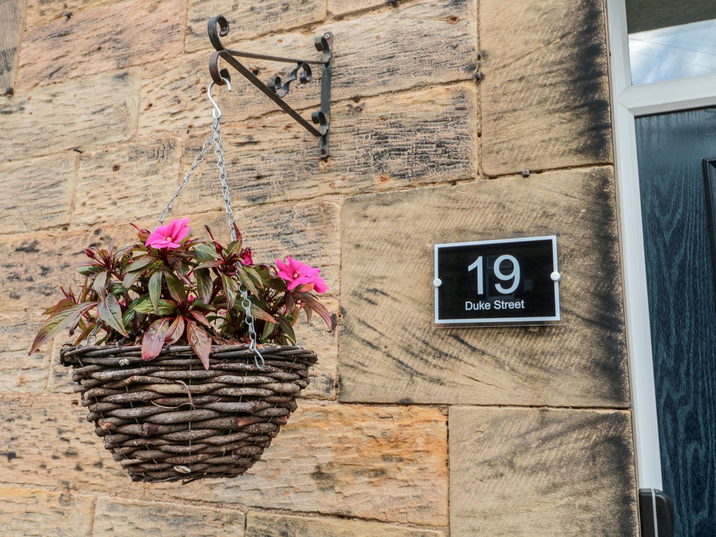 A stone wall with a hanging flower basket and a house number sign.