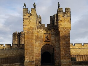 A historic stone castle with multiple towers, a central arched entrance, and statues on top. - 19 Duke Street (Alnwick)