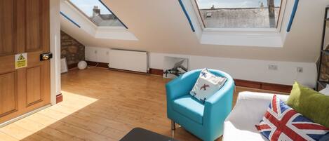 A room with a wooden floor, a blue armchair, a bed with a Union Jack pillow, and a skylight.