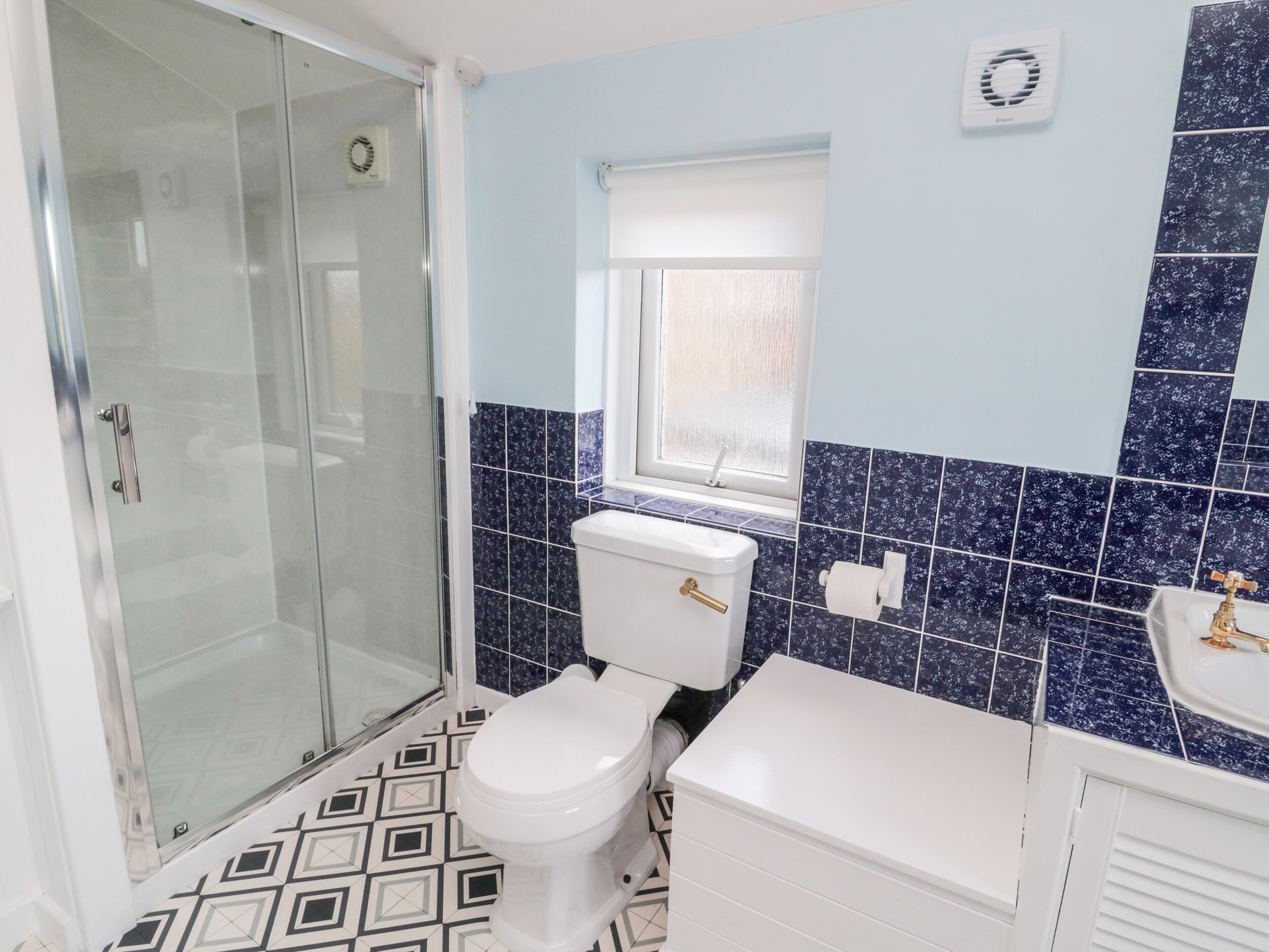 A bathroom with a glass shower enclosure, a toilet, a sink, and a window.