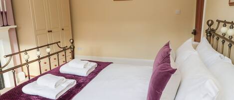 A neatly made bed with white linens and a purple throw blanket, a wooden wardrobe, and a framed picture on the wall.