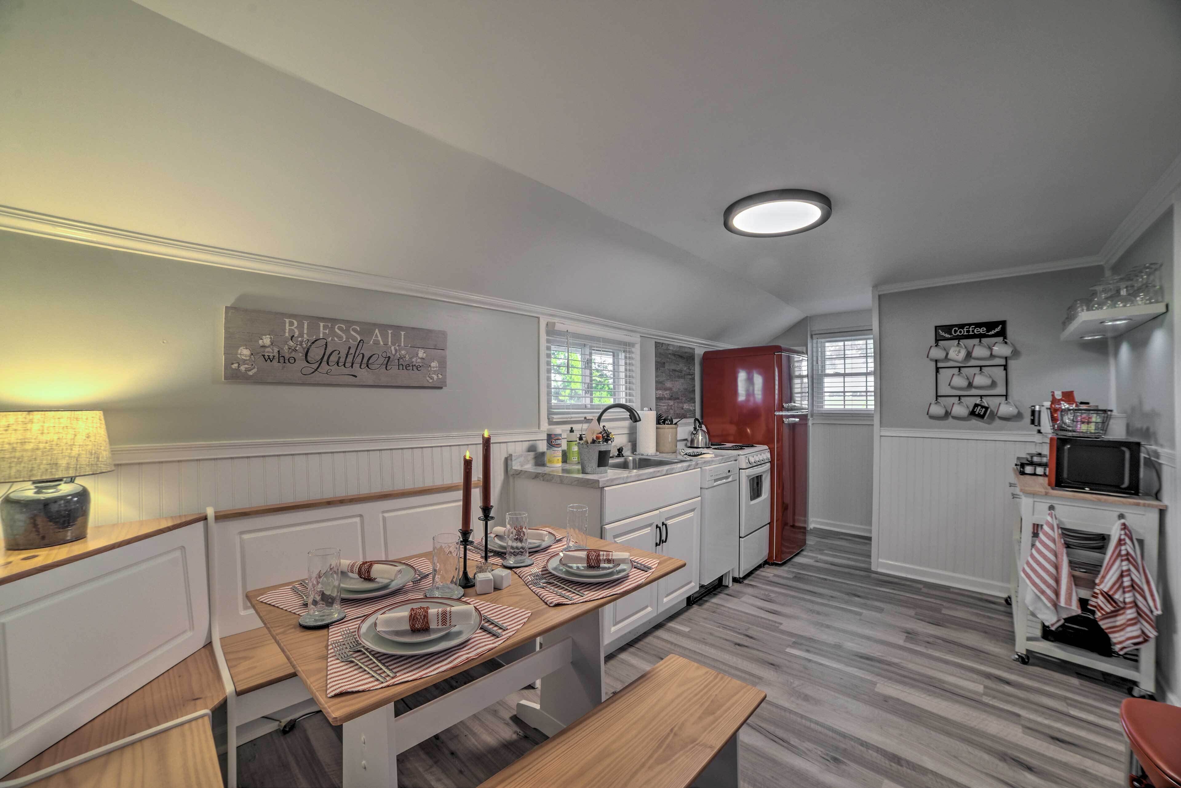Une cuisine moderne avec des meubles blancs, une table à manger en bois pour quatre personnes et un réfrigérateur rouge.