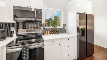 A modern kitchen with stainless steel appliances, white cabinetry, a herringbone backsplash, and a window with a view of trees.