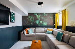 Relax in this stylish living room with a sectional sofa, flat-screen TV, and vibrant mural.