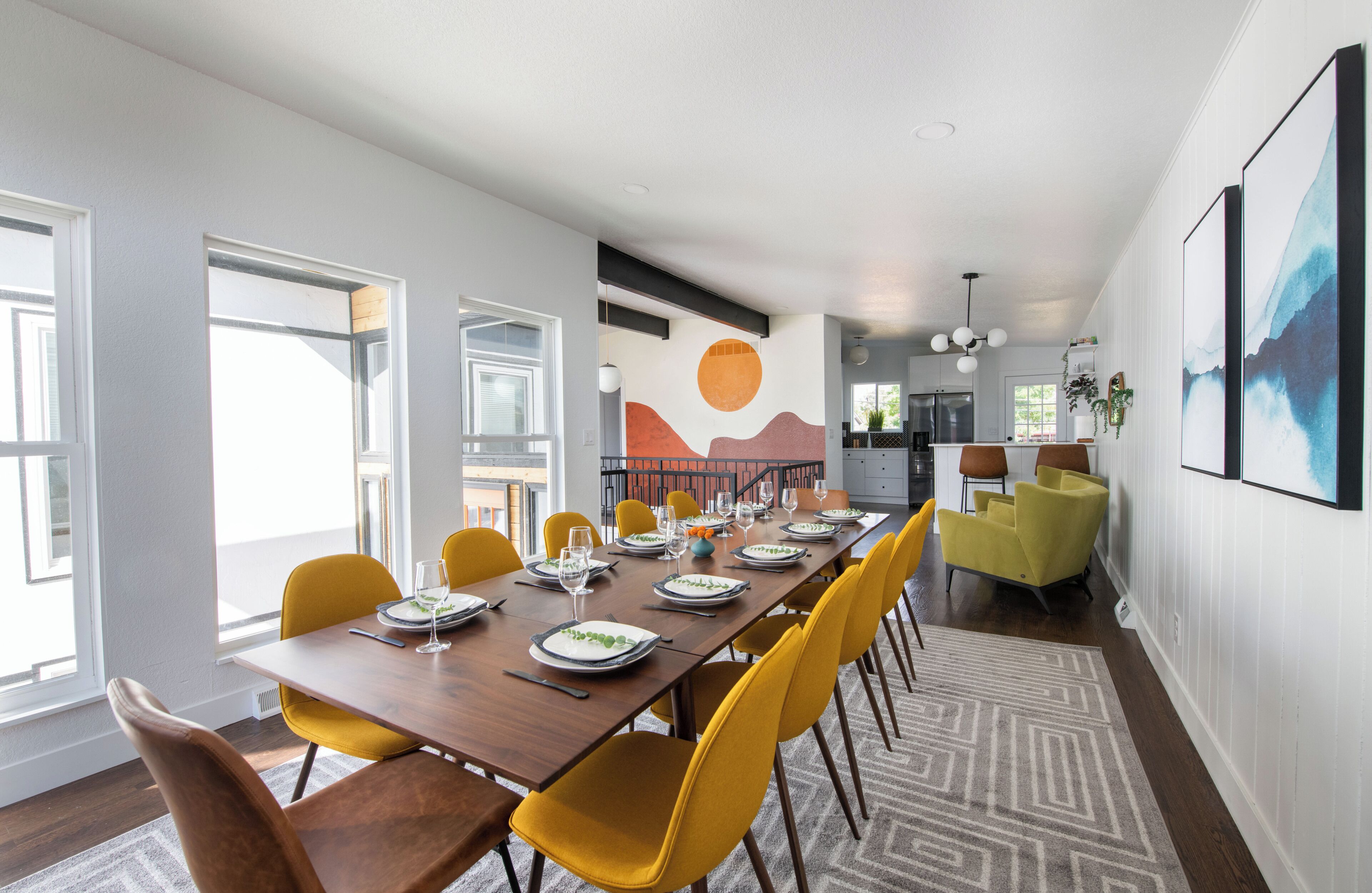 A dining area with a long table, yellow chairs, and a modern kitchen in the background.