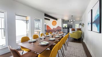 A dining area with a long table, yellow chairs, and a modern kitchen in the background.