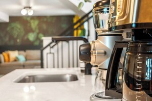Eine moderne Küche mit Kaffeemaschine, Spüle und einer Treppe im Hintergrund.