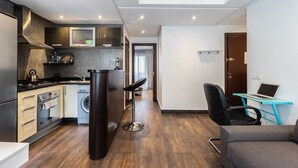 A modern kitchen with a stove, oven, and washing machine, a bar stool, a laptop on a desk, and a sofa. - Kifkif One (Bejaad)