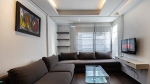 A modern living room with a sectional sofa, a glass coffee table, a mounted TV displaying 'NETFLIX', and a painting on the wall. - Kifkif One (Bejaad)