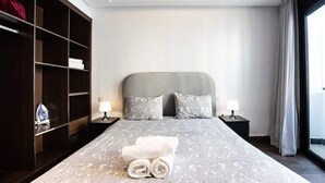 A hotel room with a large bed, two bedside tables with lamps, a wardrobe, and a view through a large window. - Kifkif One (Bejaad)