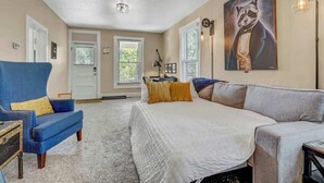 A bedroom with a large bed, a blue armchair, a grey sofa, and a painting of a raccoon on the wall. - Game Parlour! Downtown Workspace BBQ Fire Pit (Colorado Springs)