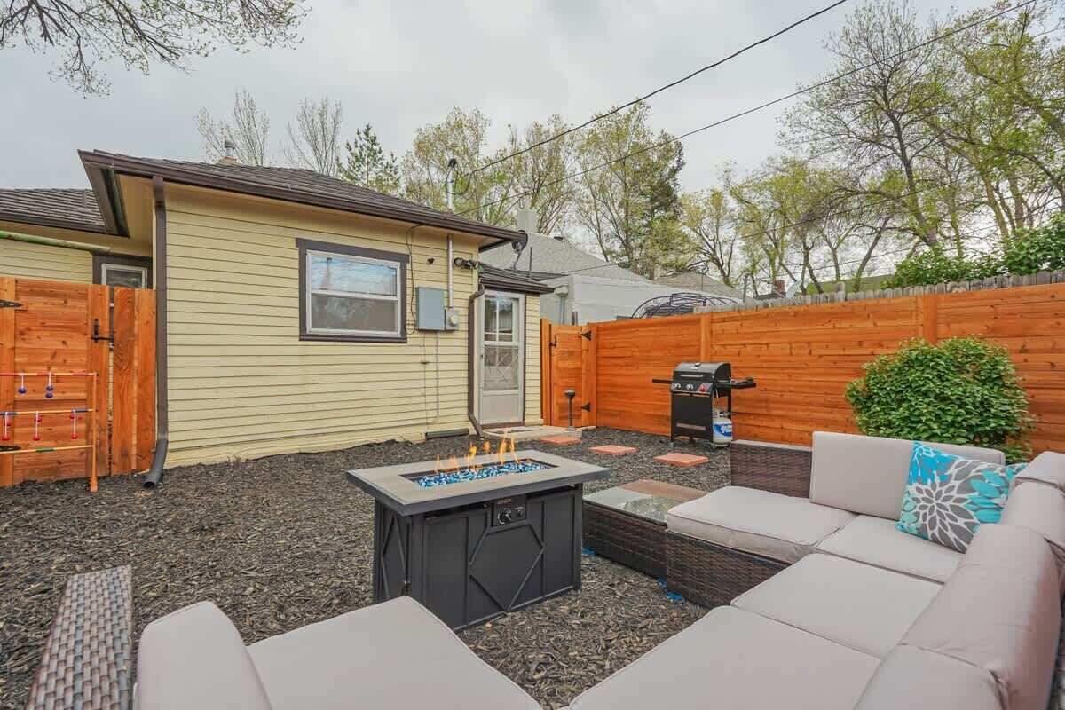 Un patio trasero con una fogata, asientos al aire libre, una valla de madera y una parrilla.