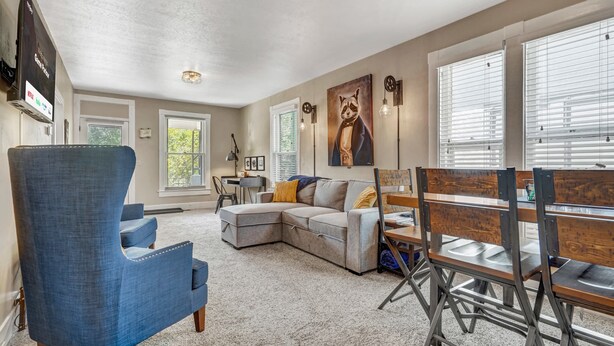 A spacious living room with a sectional sofa, a blue armchair, and a dining area with a wooden table and chairs. - Game Parlour! Downtown Workspace BBQ Fire Pit (Colorado Springs)