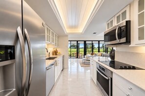 A modern kitchen with stainless steel appliances, white cabinetry, and a view of a green landscape through large windows.