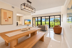 A modern living room with a wooden dining table, a sofa, and a large window offering a view of a golf course.