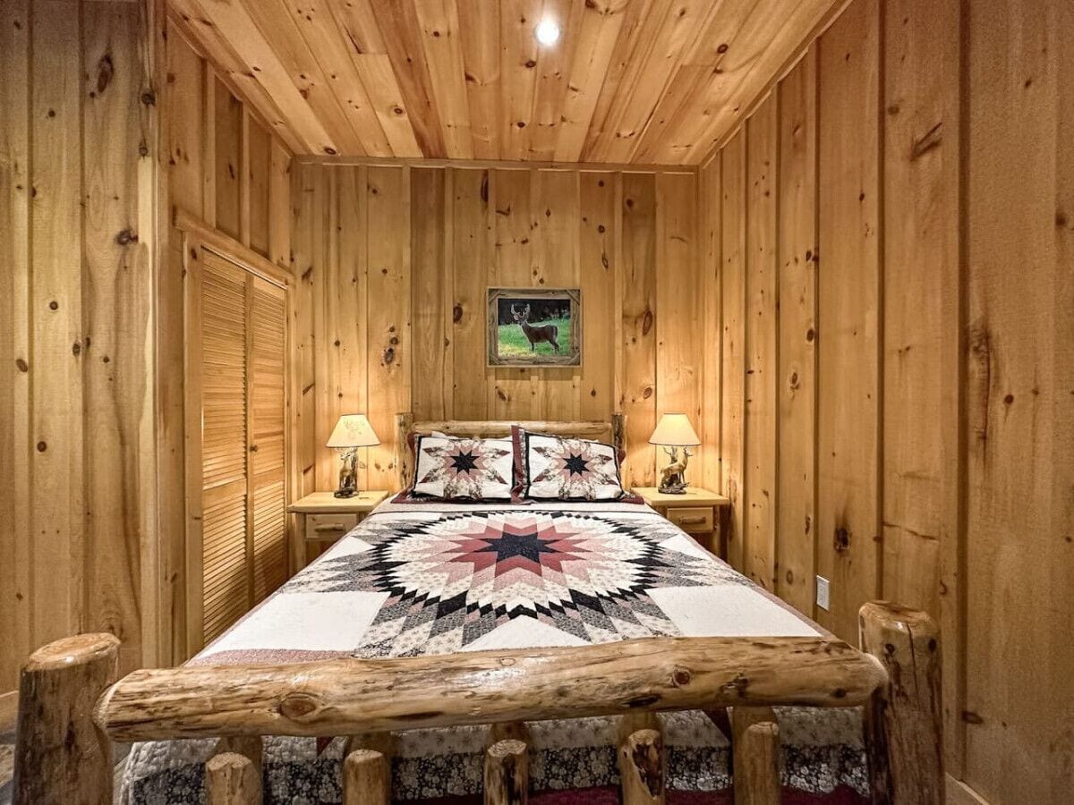 Une chambre à coucher dans un chalet en bois, avec un lit, deux lampes de chevet, une courtepointe et un tableau encadré au mur.