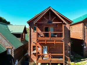 A two-story log cabin with a balcony on the second floor, a green roof, and a sign that reads "Love the Lakes." - Gatlinburg Cabin w/ Indoor Heated Pool & Hot Tub (Gatlinburg)