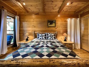 A cozy wooden cabin bedroom with a checkered bedspread, two bedside lamps, and a framed picture on the wall. - Gatlinburg Cabin w/ Indoor Heated Pool & Hot Tub (Gatlinburg)