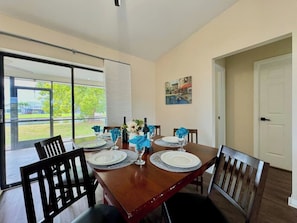 Un coin repas avec une table en bois dressée pour quatre personnes, des chaises et une vue sur une pelouse, visible à travers des portes vitrées.