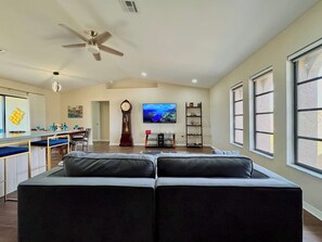 A spacious living area with a large sofa, a television, and a dining area with a kitchen in the background.