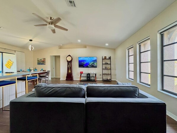 A spacious living area with a large sofa, a television, and a dining area with a kitchen in the background.