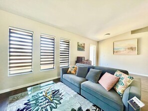 A living room with a sofa, patterned rug, and three windows with blinds.