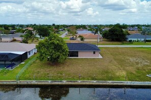 Un quartier résidentiel avec des maisons, un grand arbre et une étendue d’eau au premier plan.