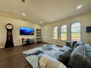 A living room with a sofa, a flat-screen TV, a clock, and a large window.