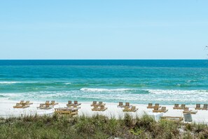 Une plage bordée de rangées de chaises longues et de tables en bois, une étendue de sable et l’océan en toile de fond.