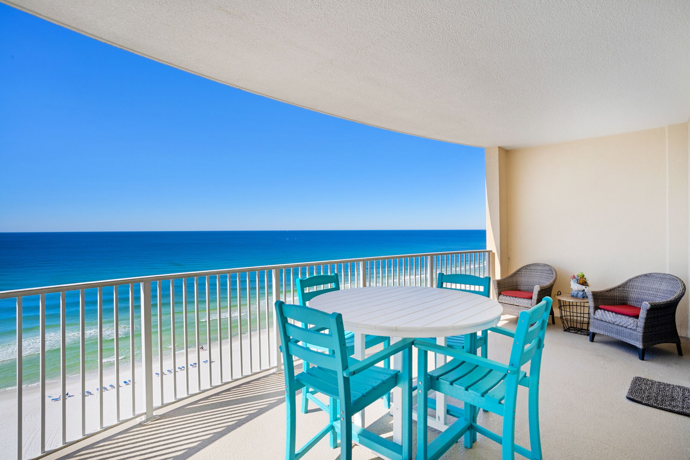 A balcony with a view of the ocean, a round table with chairs, and wicker furniture.