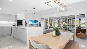 Una cocina moderna con armarios blancos, una mesa de comedor de madera y un televisor en la isla.