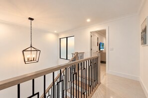 A modern interior with a staircase, a hanging light fixture, and a door leading to another room.