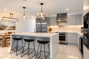 Een moderne keuken met een centraal eiland, barstoelen, roestvrijstalen apparatuur en hanglampen.
