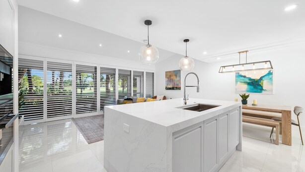 Una cocina moderna con una isla grande, armarios blancos e iluminación colgante.